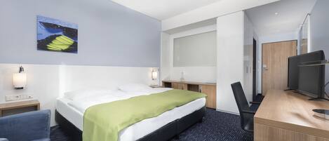 A hotel room with a bed, a desk, a chair, a TV, and a painting on the wall.