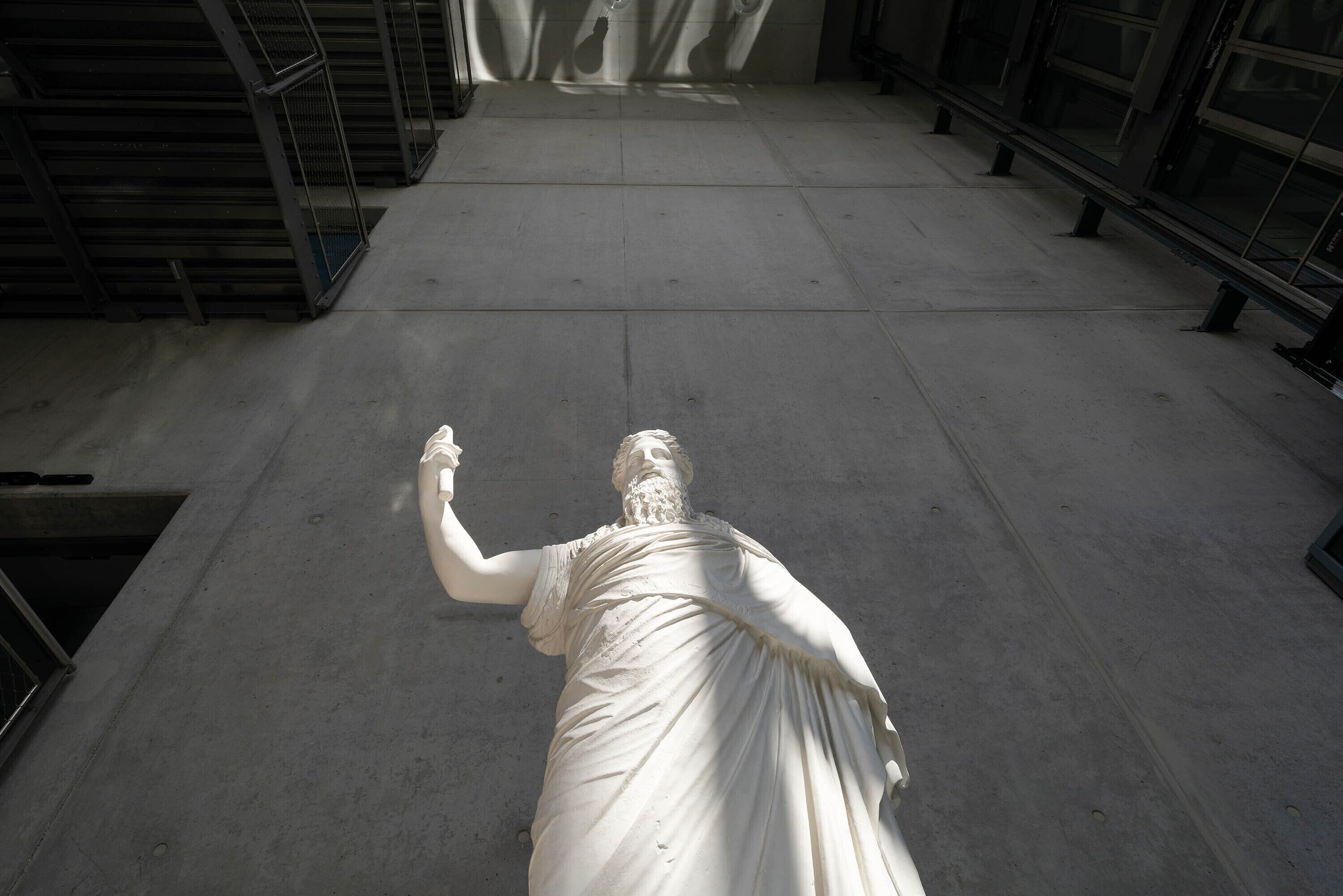 A marble statue in a spacious, modern indoor setting with concrete floors and metal railings.