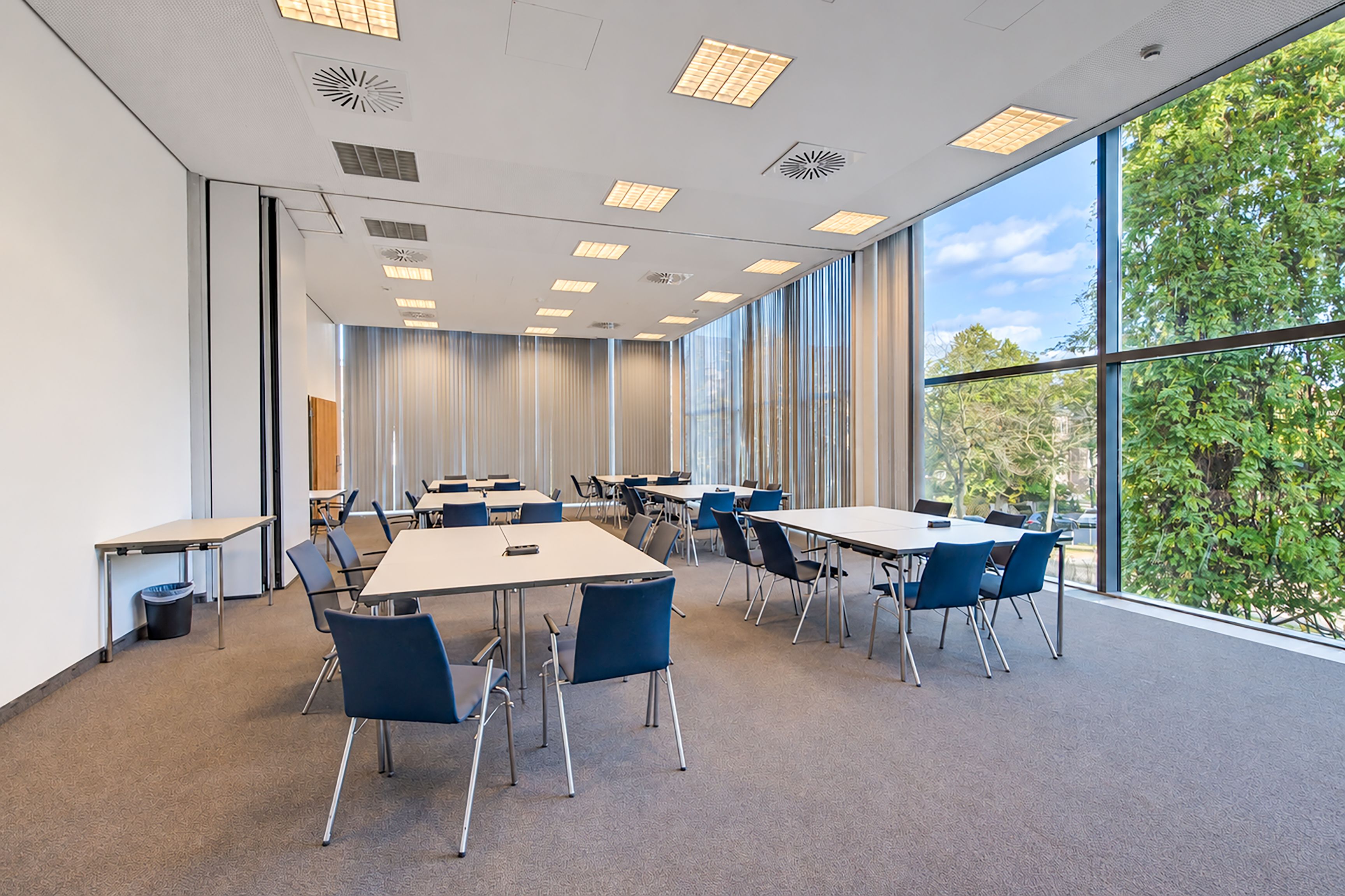 Une salle de conférence équipée de tables et de chaises, de grandes fenêtres et offrant une vue sur les arbres.