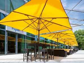 Outdoor seating with yellow umbrellas, a glass building, and a sign for "Papillon Restaurant". - Seminaris Sunday Campus Hotel Berlin (Berlin)