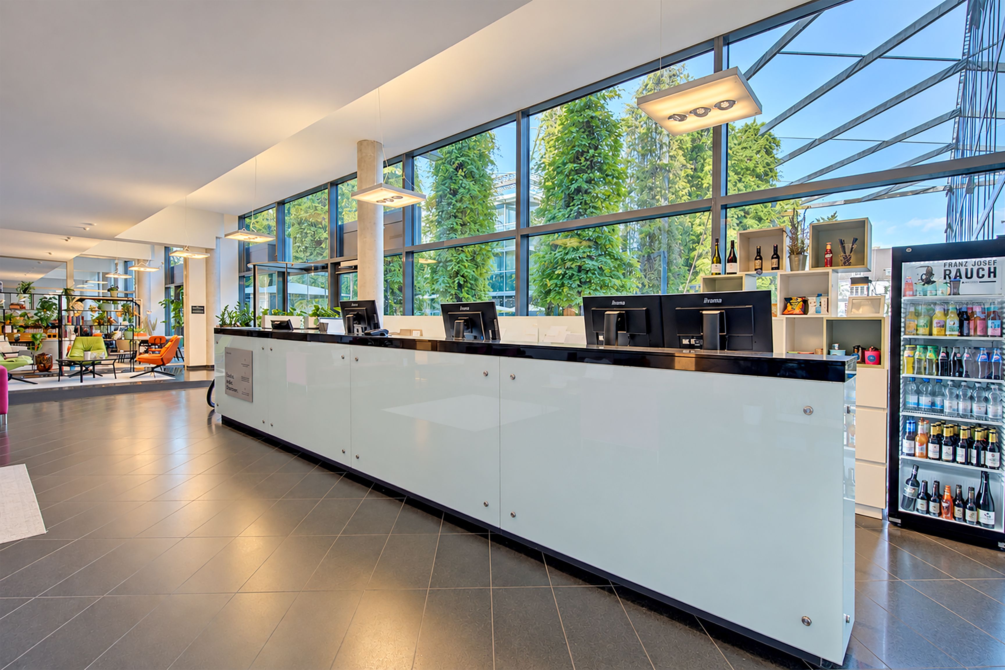 A modern interior with a long reception desk, large windows, and a variety of seating areas.