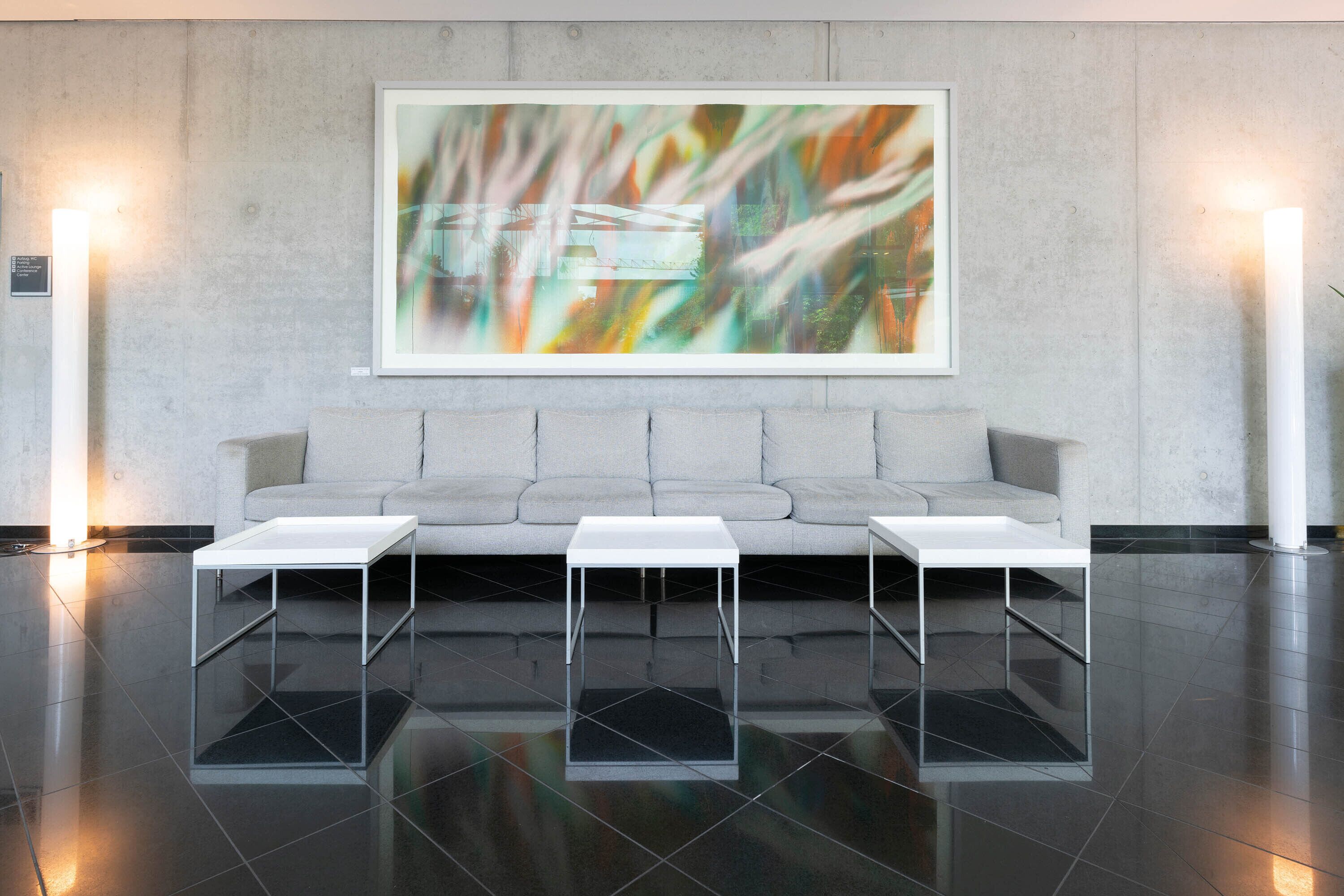 A modern interior with a grey sofa, three white side tables, and a large abstract painting on the wall.