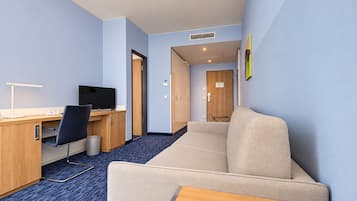 Hotellihuone, jossa on työpöytä, tuoli, televisio, sohva ja pieni pöytä.