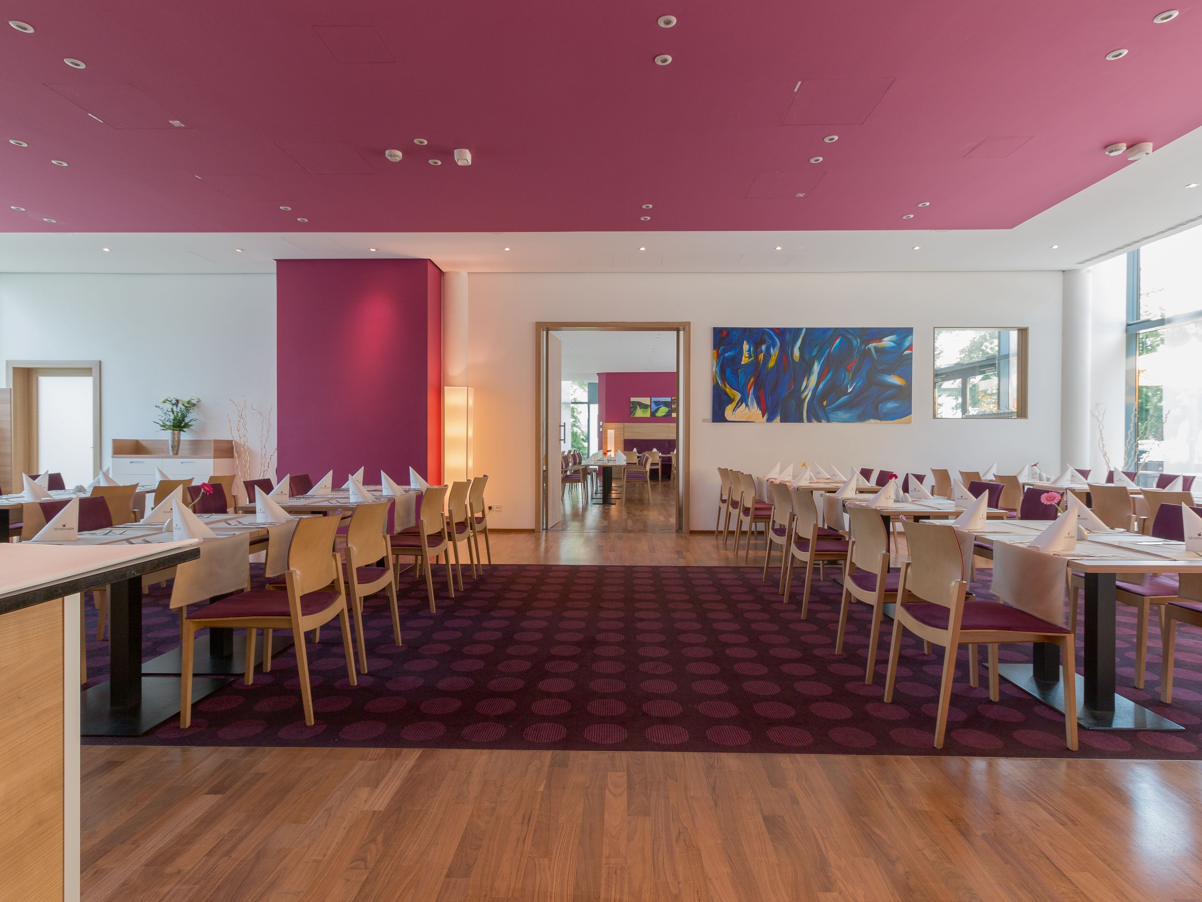 Un comedor moderno con mesas y sillas de madera, una alfombra estampada y un techo rosa.