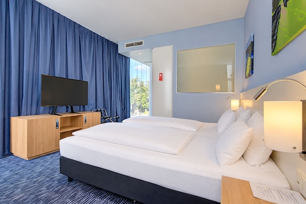 Habitación de hotel con una cama grande, televisión, escritorio y ventana con cortinas.