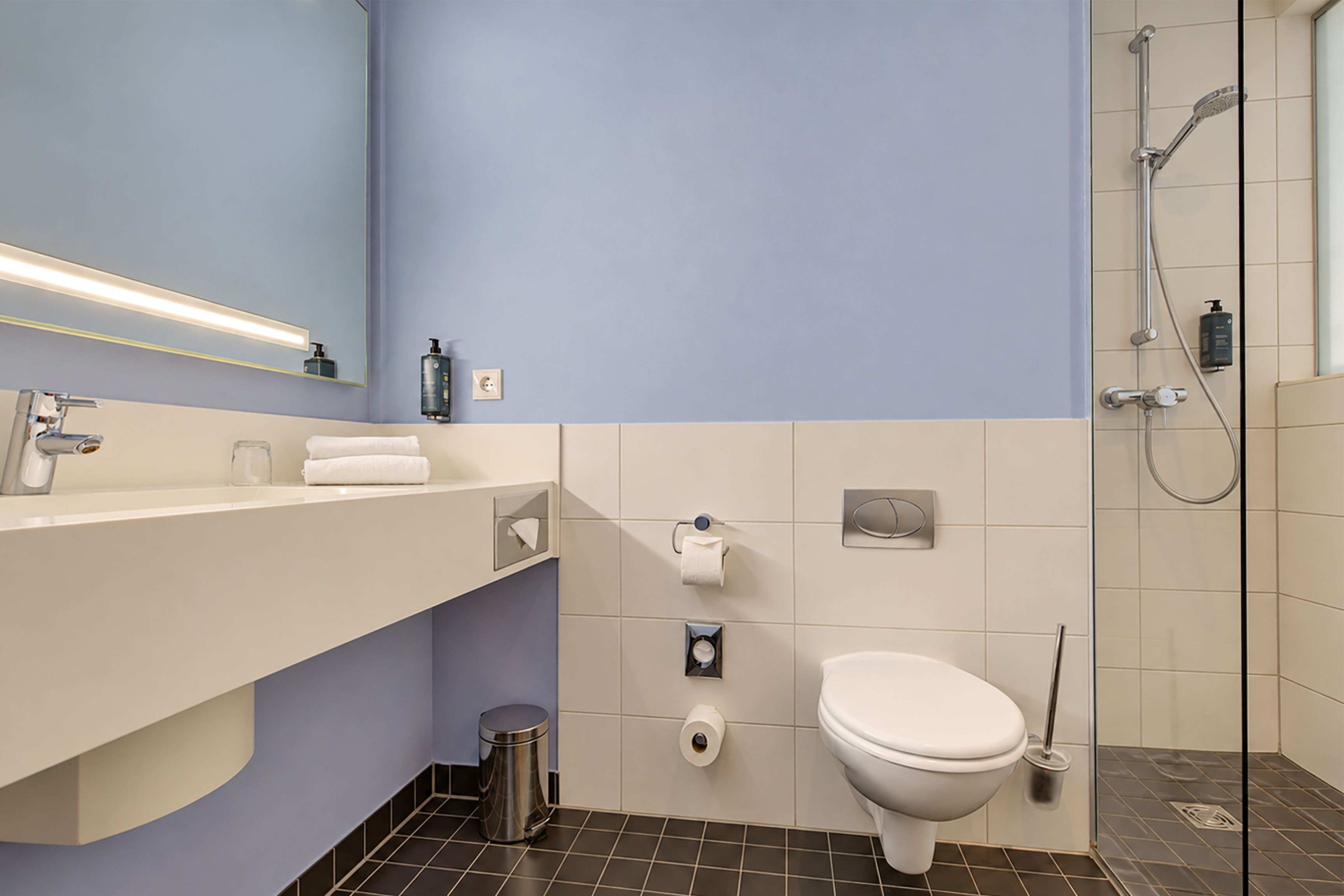 A modern bathroom with a white sink, mirror, and toilet. There is a shower area with a glass door and a handheld showerhead.