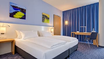 Ein Hotelzimmer mit einem Doppelbett, einem Schreibtisch, zwei Wandlampen und zwei Bildern.