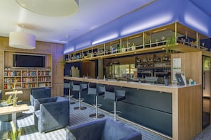A modern bar area with a high bar, seating with stools, a TV, and a bookshelf with books. - Seminaris Sunday Campus Hotel Berlin (Berlin)