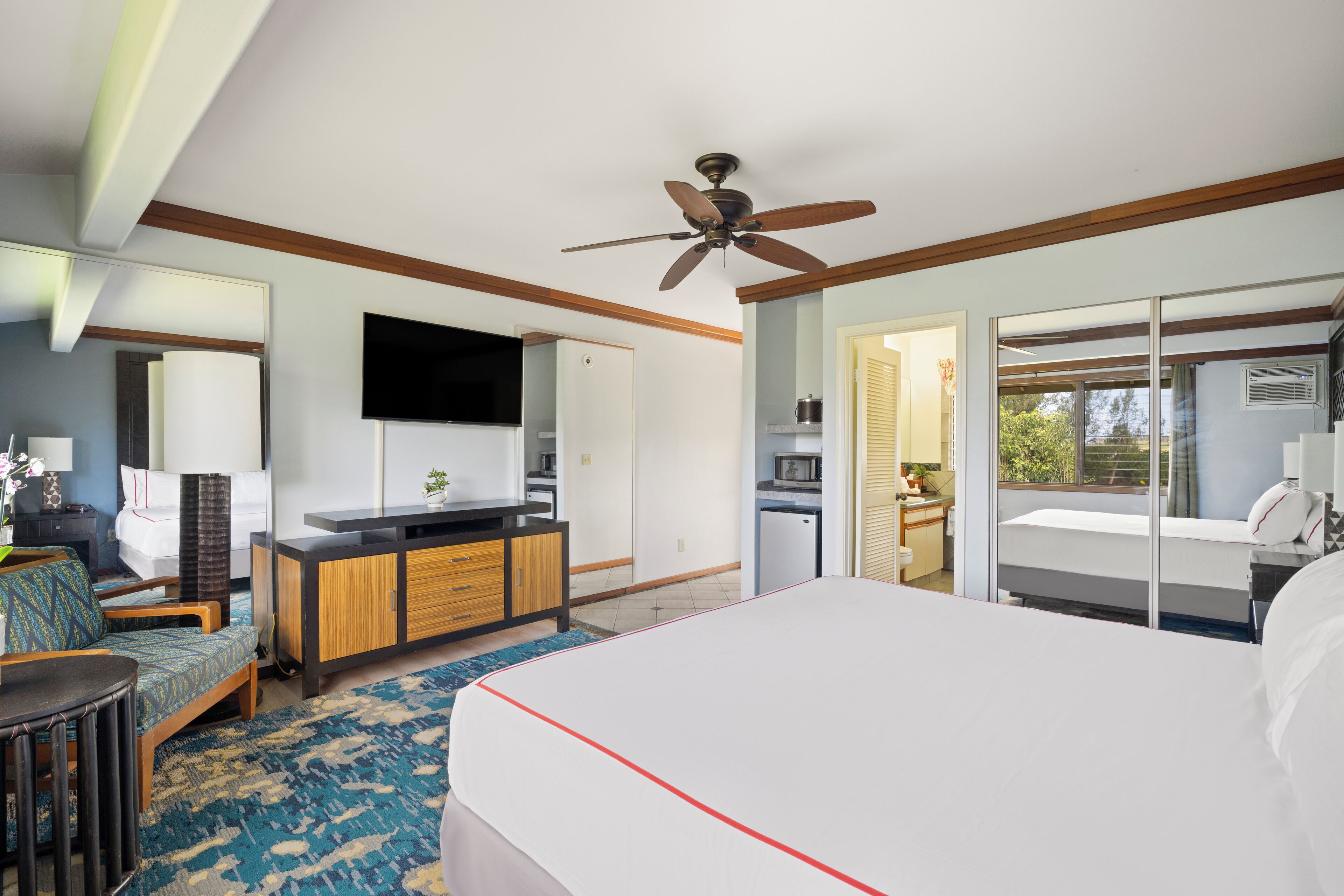 A hotel room with a bed, a desk, a chair, a TV, and a balcony with a view.