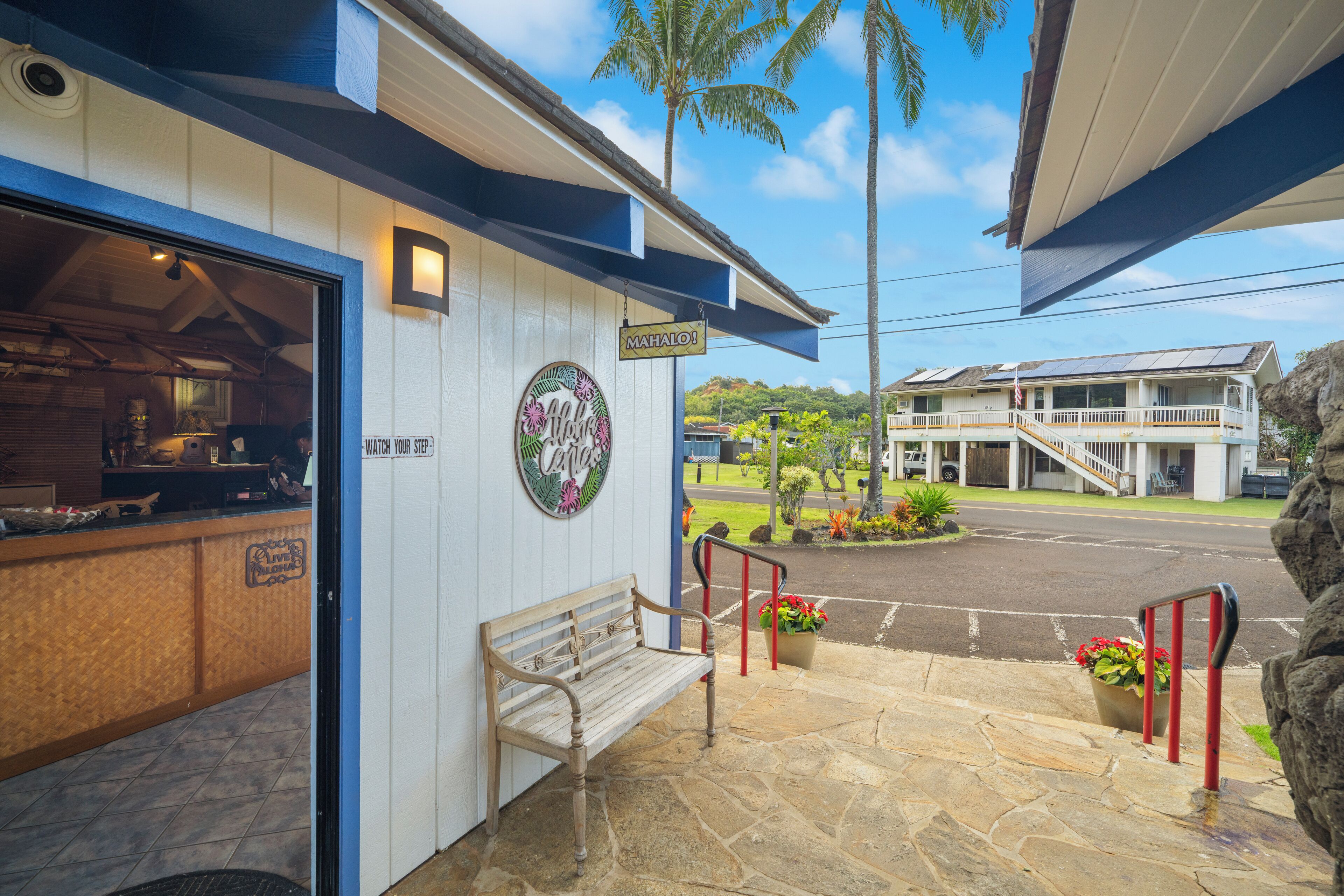 A building with a wooden bench outside, a sign reading "MAHALO!", and a stone-paved entrance.