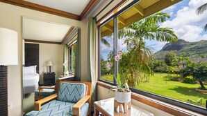 Une chambre d’hôtel avec une grande fenêtre, un lit, une chaise, une petite table et une plante en pot.