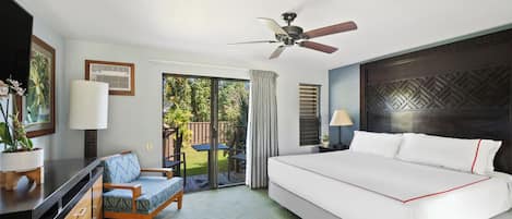 A hotel room with a large bed, a ceiling fan, a desk with a lamp, a chair, and a view of the outdoors.