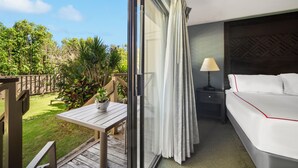 Une chambre d’hôtel avec un balcon, un lit avec une literie blanche, une table de chevet avec une lampe, et une vue sur un jardin.