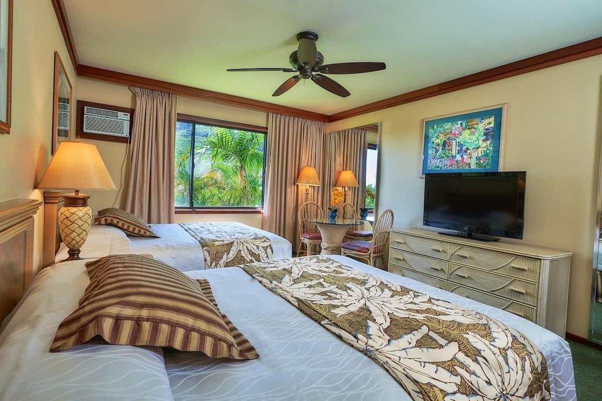A hotel room with two beds, a ceiling fan, a TV, and a window with curtains.