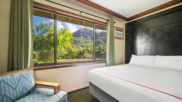 A hotel room with a large bed, a sofa, and a window with a view of lush greenery and mountains.