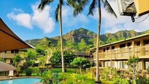 A hotel courtyard with a swimming pool, palm trees, and a mountainous backdrop.