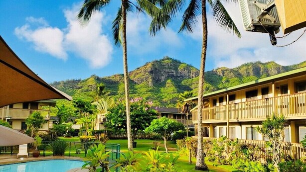 Une cour d’hôtel avec une piscine, des palmiers et une chaîne de montagnes en arrière-plan.