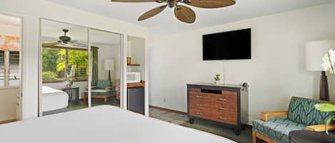 Ein Hotelzimmer mit einem großen Bett, einem Deckenventilator, einem Flachbildfernseher, einer Holzkommode, einem Sofa und Blick ins Freie.
