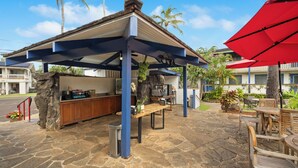 A covered outdoor seating area with stone flooring, wooden furniture, and a red umbrella.
