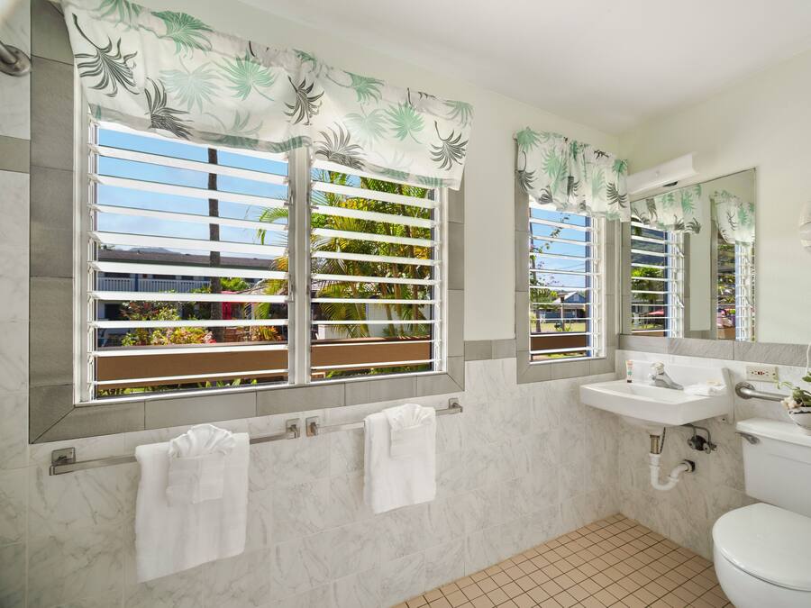 A bathroom with two windows, a sink, a toilet, and a mirror.