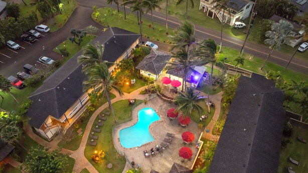 An aerial view of a resort with a swimming pool, palm trees, and outdoor seating areas.