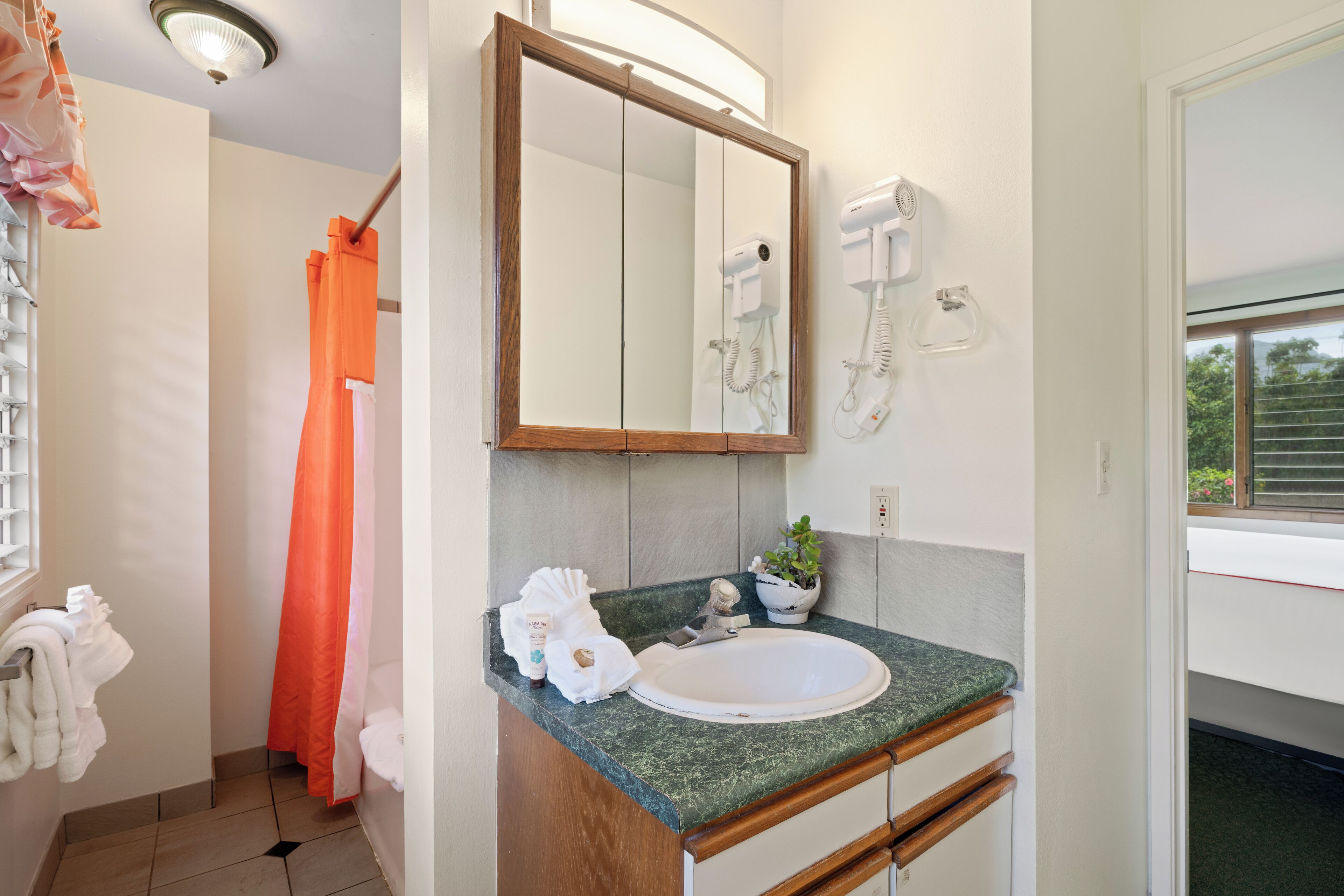 Un baño con lavamanos, espejo, toallero y cortina de ducha.