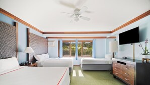 A hotel room with two beds, a desk, a TV, and a view of the outdoors.