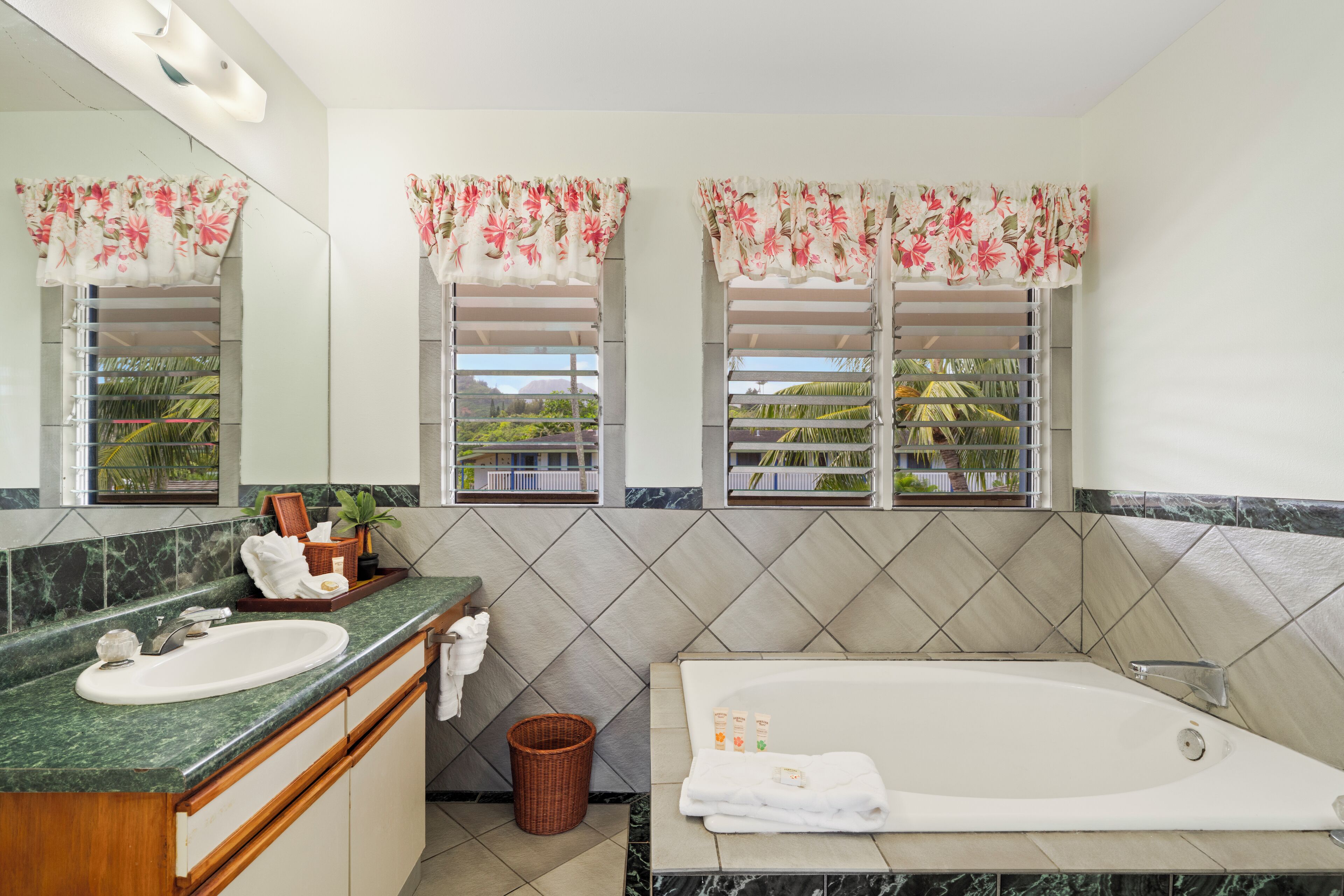 A bathroom with a marble sink, a bathtub, and two windows with floral curtains.