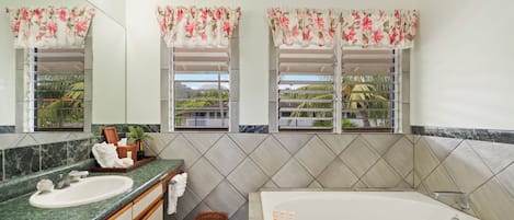 A bathroom with a marble sink, a bathtub, and two windows with floral curtains.