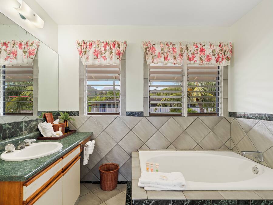 A bathroom with a marble sink, a bathtub, and two windows with floral curtains.