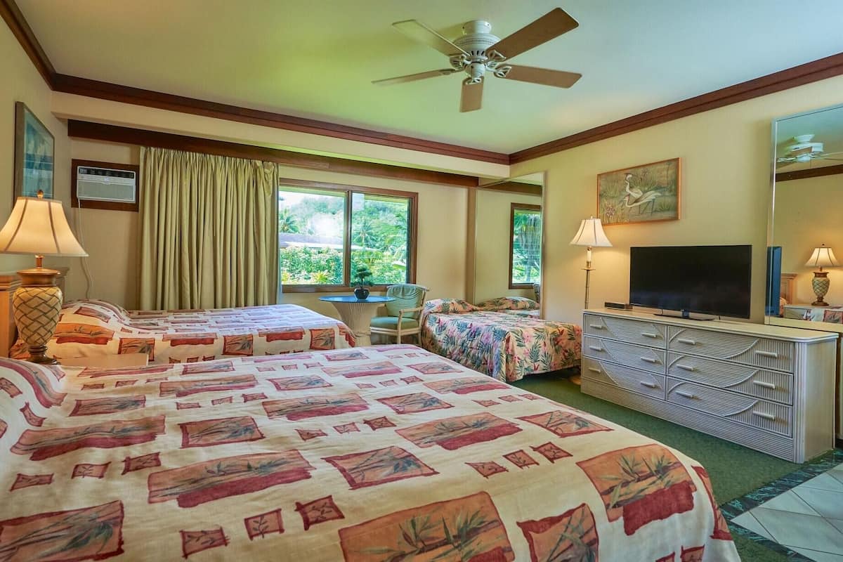 A hotel room with two beds, a ceiling fan, a TV, a dresser, and a window with curtains.