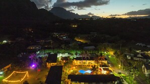 Un complexe hôtelier doté d’une piscine, de sentiers illuminés et offrant une vue sur les montagnes au crépuscule.