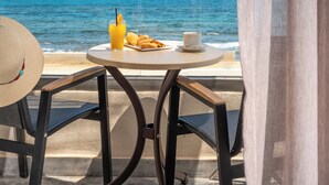 Un balcón con una mesa, una silla, un sombrero, un vaso de zumo de naranja, croissants y una taza, con vistas al mar.
