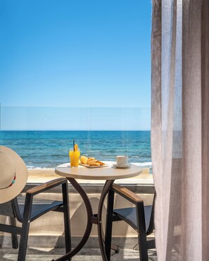 A balcony with a table, a chair, a hat, a glass of orange juice, croissants, and a cup, overlooking the sea.