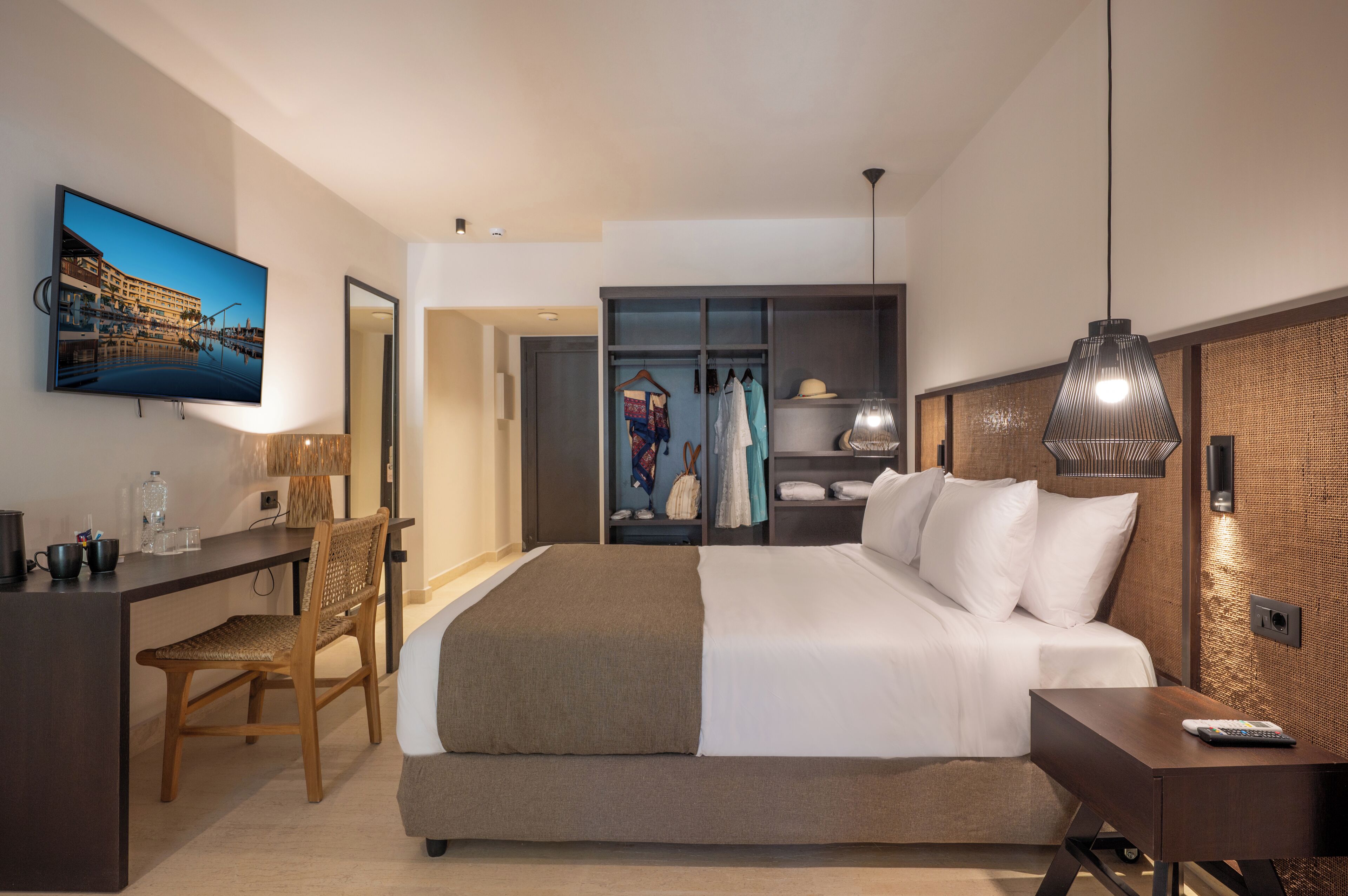 Una habitación de hotel moderna con cama, escritorio, silla, televisor, armario y perchero.