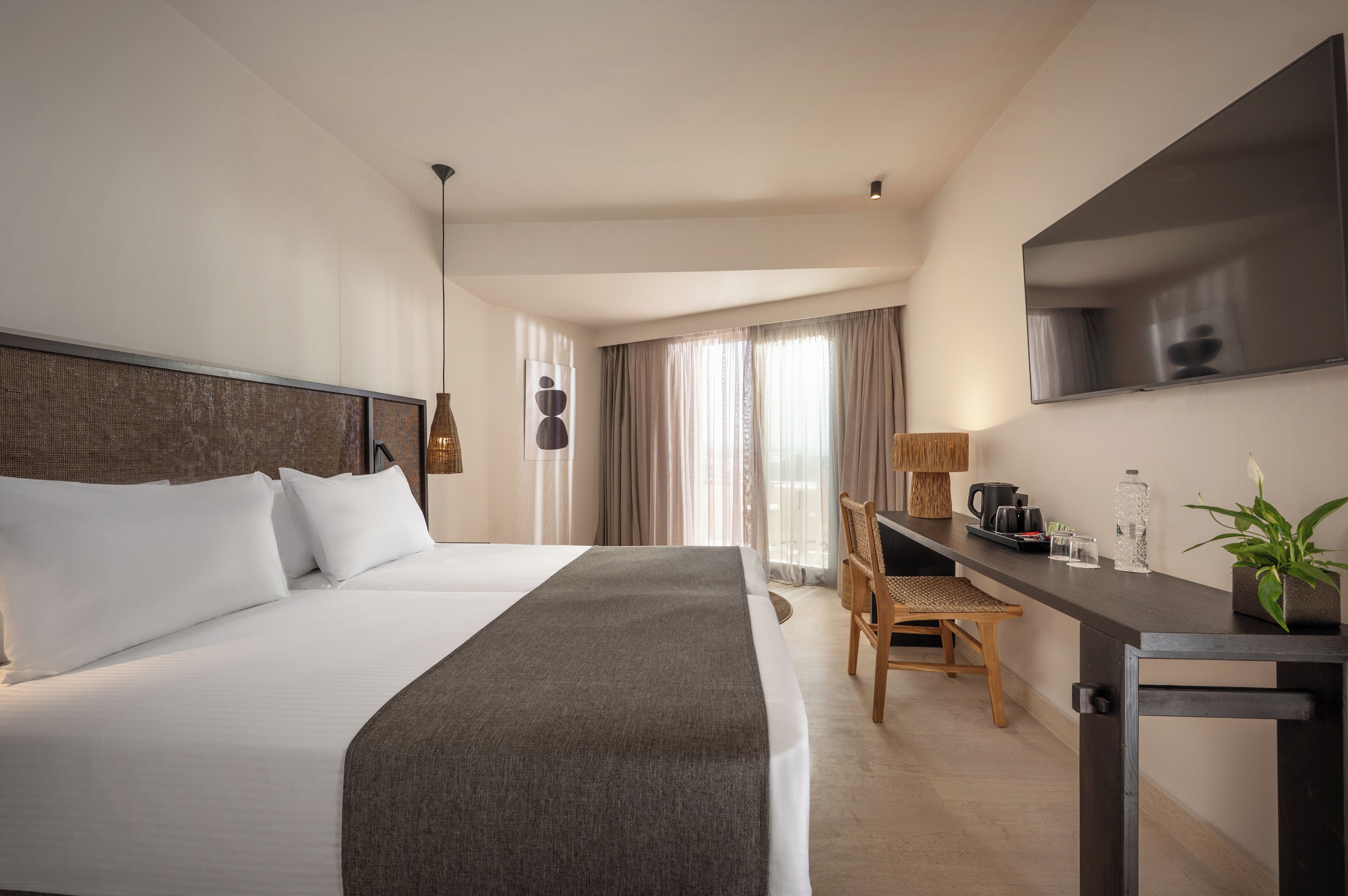 Habitación de hotel con una cama grande, un escritorio, una silla, un televisor y una ventana con cortinas.