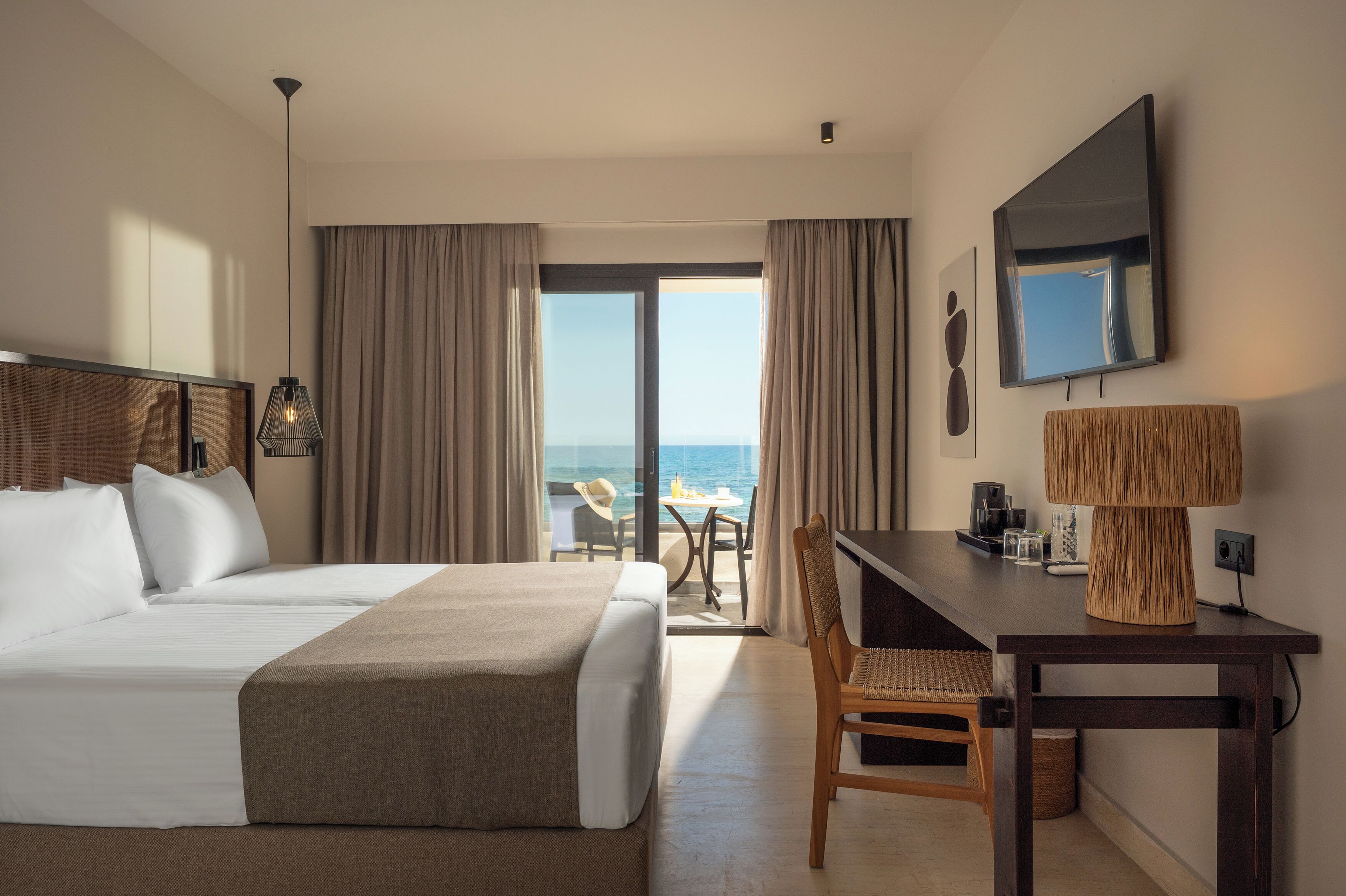 A hotel room with a bed, a desk, a chair, a TV, and a view of the ocean.
