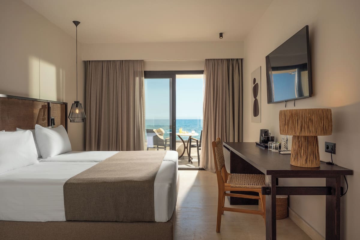 A hotel room with a bed, a desk, a chair, a TV, and a view of the ocean.