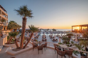 Kattoterassi, jossa on ulkotilaa istumiseen, palmuja ja upea näkymä merelle auringonlaskun aikaan.