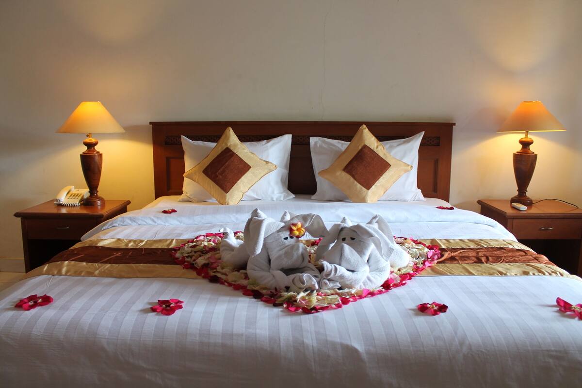 A hotel room with a neatly made bed, two bedside tables with lamps, and a wooden headboard.