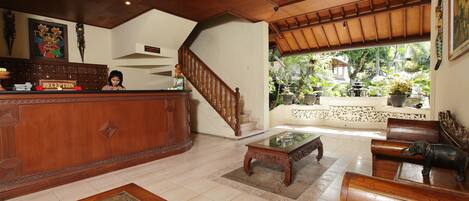 A reception area with a wooden reception desk, a staircase, and a view of the garden through a glass door.