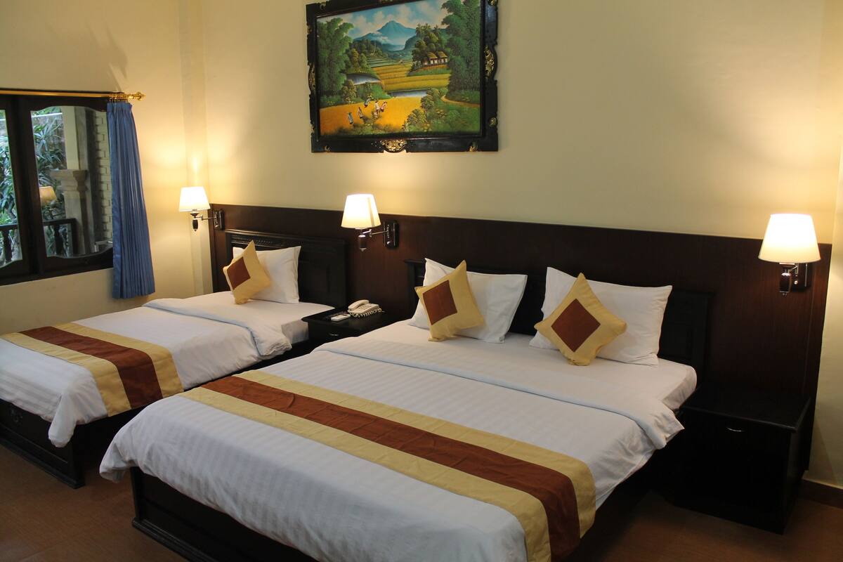 A hotel room with two beds, each with a headboard, bedside lamps, and a painting above the beds.
