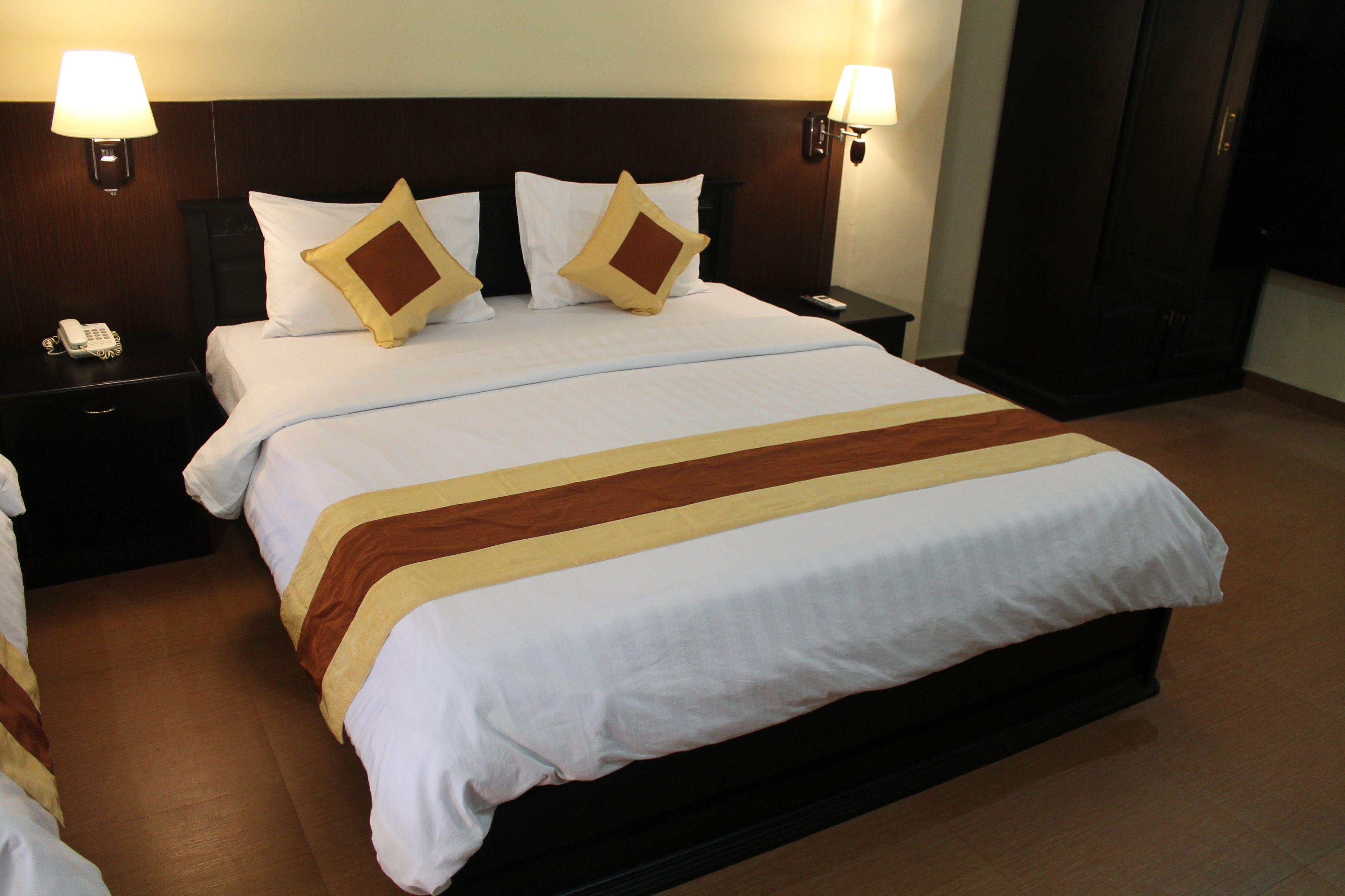 A neatly made bed with white and brown linens, two bedside tables with lamps, and a dark wooden headboard.