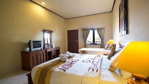 A hotel room with a bed, a desk with a television, a wardrobe, and a window with curtains. - Balisandy Resort (Kuta)