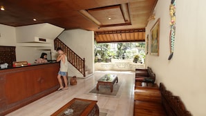 A reception area with a wooden reception desk, a staircase, and a view of the garden. - Balisandy Resort (Kuta)