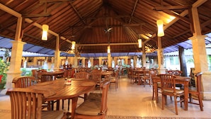 A spacious covered dining area with wooden tables and chairs, a high ceiling with exposed beams, and hanging pendant lights. - Balisandy Resort (Kuta)
