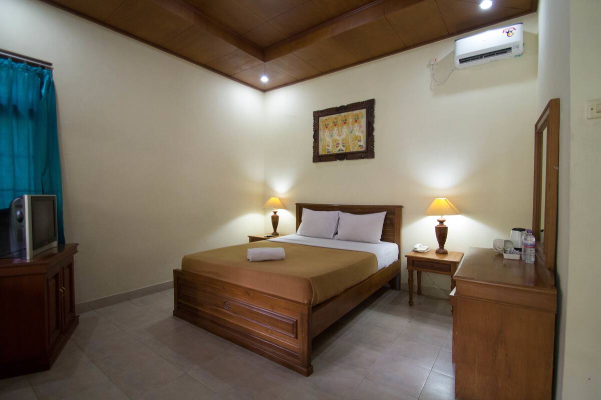 A hotel room with a wooden bed, bedside lamps, a TV, a desk, and a mirror.