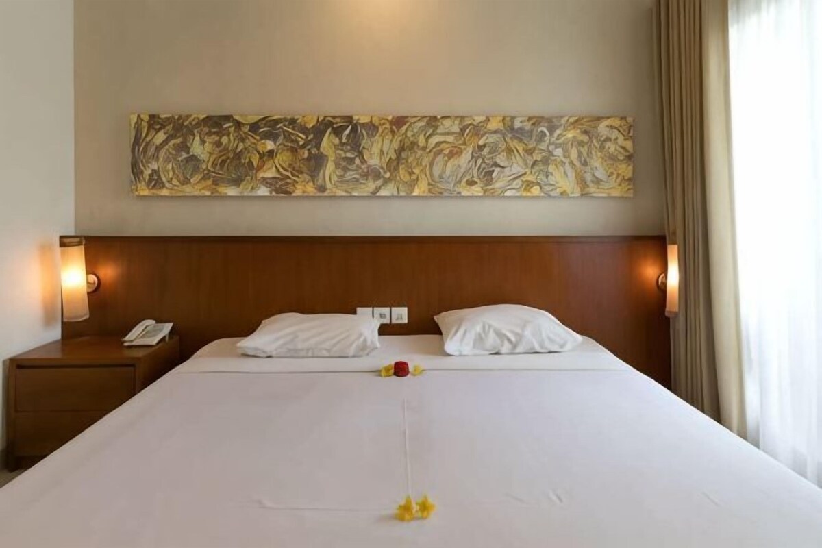 A hotel room with a large bed, a wooden headboard, a wall-mounted painting, and bedside lamps.