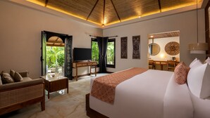 A well-lit bedroom with a large bed, a wooden desk, a television, and a view of greenery outside. - Tonys Villas & Resort (Keroboken Kelod)