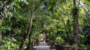 A pathway surrounded by lush greenery and palm trees, leading to a structure with a thatched roof. - Tonys Villas & Resort (Keroboken Kelod)